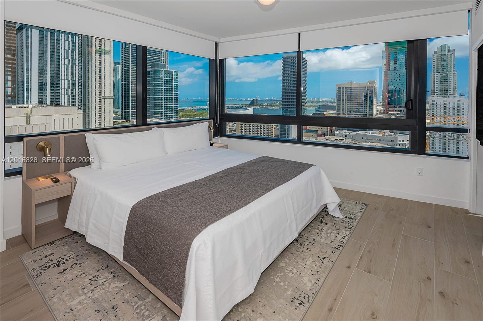 A bedroom features a bed with a gray runner, light wood floors, and floor-to-ceiling windows — 225 N Miami Ave # 2801, Miami FL 33128, MIAMI, FL