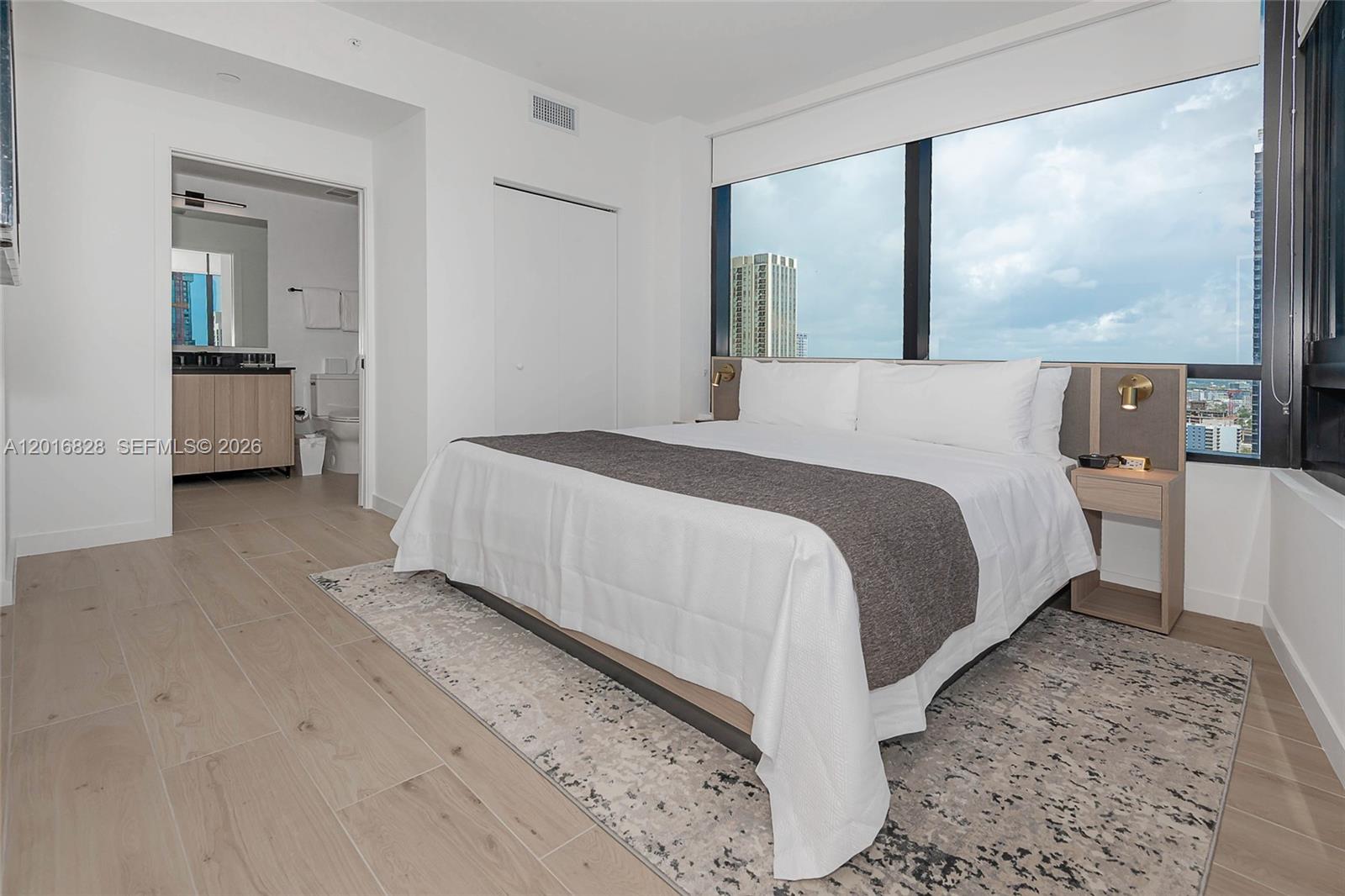 A modern bedroom features a king bed, wood-look tile flooring, and floor-to-ceiling windows — 225 N Miami Ave # 2801, Miami FL 33128, MIAMI, FL