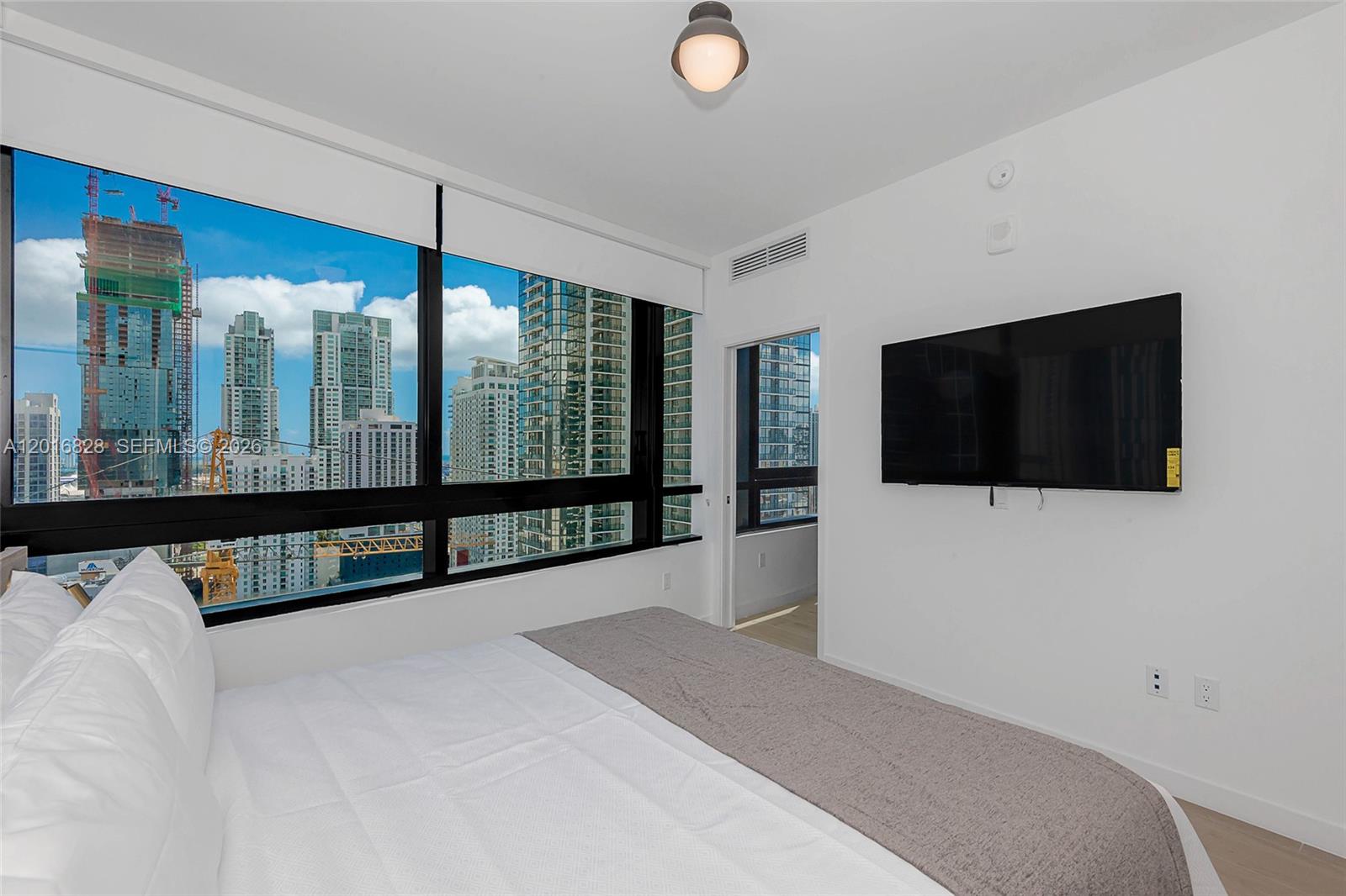 A bedroom features a bed, a wall-mounted television, and floor-to-ceiling windows overlooking a city skyline — 225 N Miami Ave # 2801, Miami FL 33128, MIAMI, FL