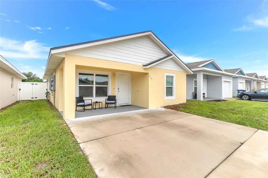 A yellow single-story house features a covered front porch, a concrete driveway, and white trim — 1502 LAS VILLAS BOULEVARD, SEBRING, FL