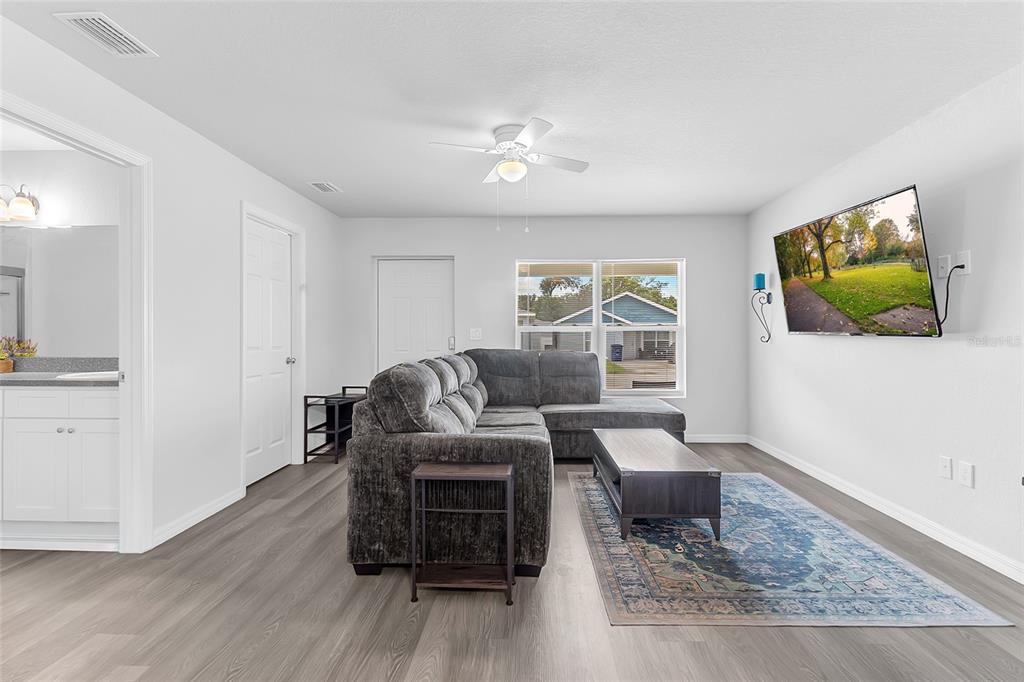 A living room features gray wood-look flooring, a sectional sofa, and a wall-mounted television — 1502 LAS VILLAS BOULEVARD, SEBRING, FL