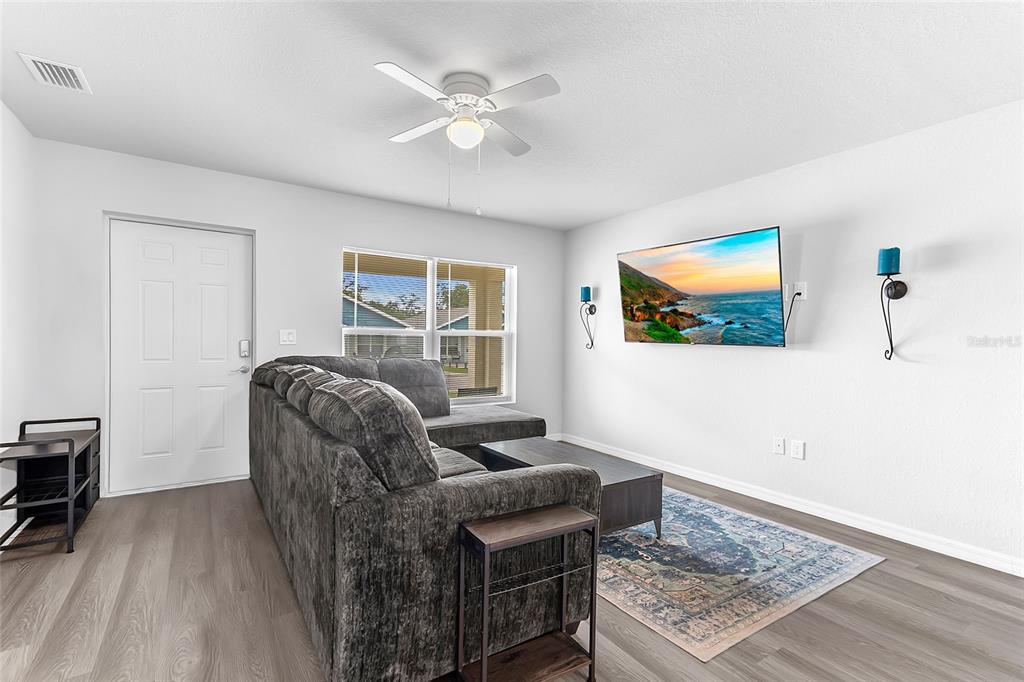 A living room features a grey sectional sofa, a wall-mounted television, and light wood flooring — 1502 LAS VILLAS BOULEVARD, SEBRING, FL