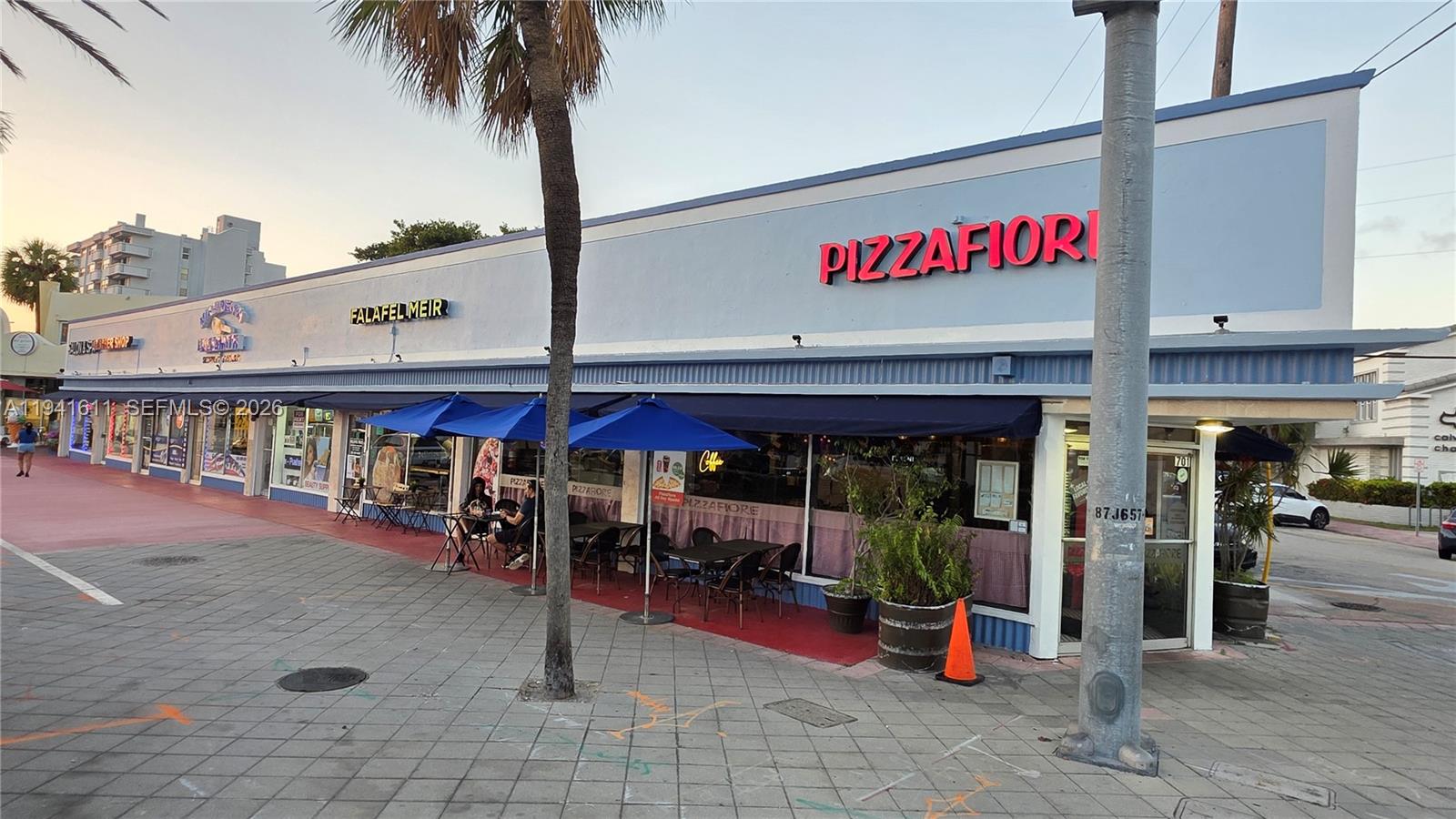 An exterior view of a commercial strip mall featuring a pizza restaurant with outdoor seating — 707 71st St, Miami Beach FL 33141, MIAMI BEACH, FL