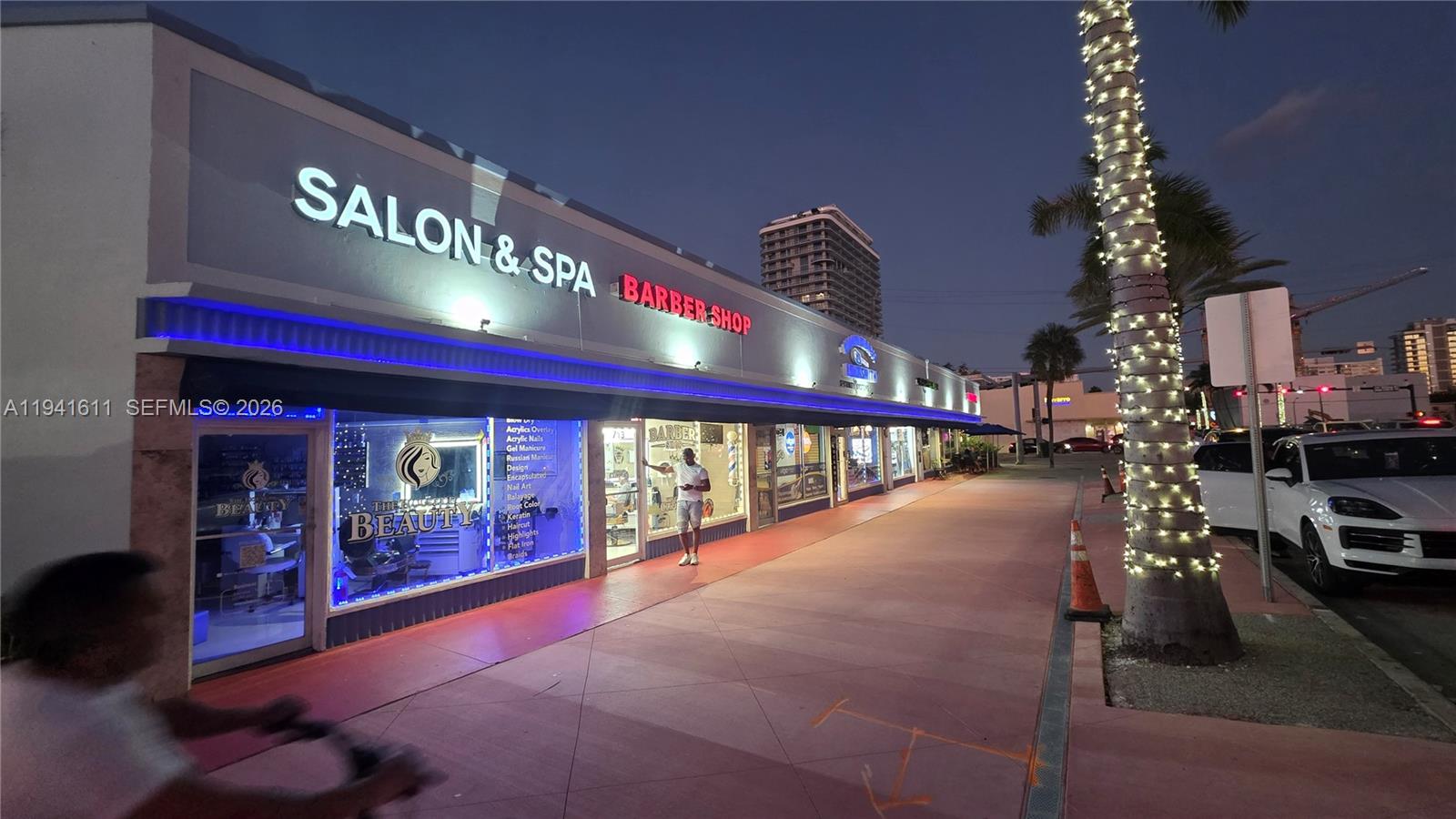 A storefront with a salon, spa, and barber shop at dusk with a lit palm tree — 707 71st St, Miami Beach FL 33141, MIAMI BEACH, FL