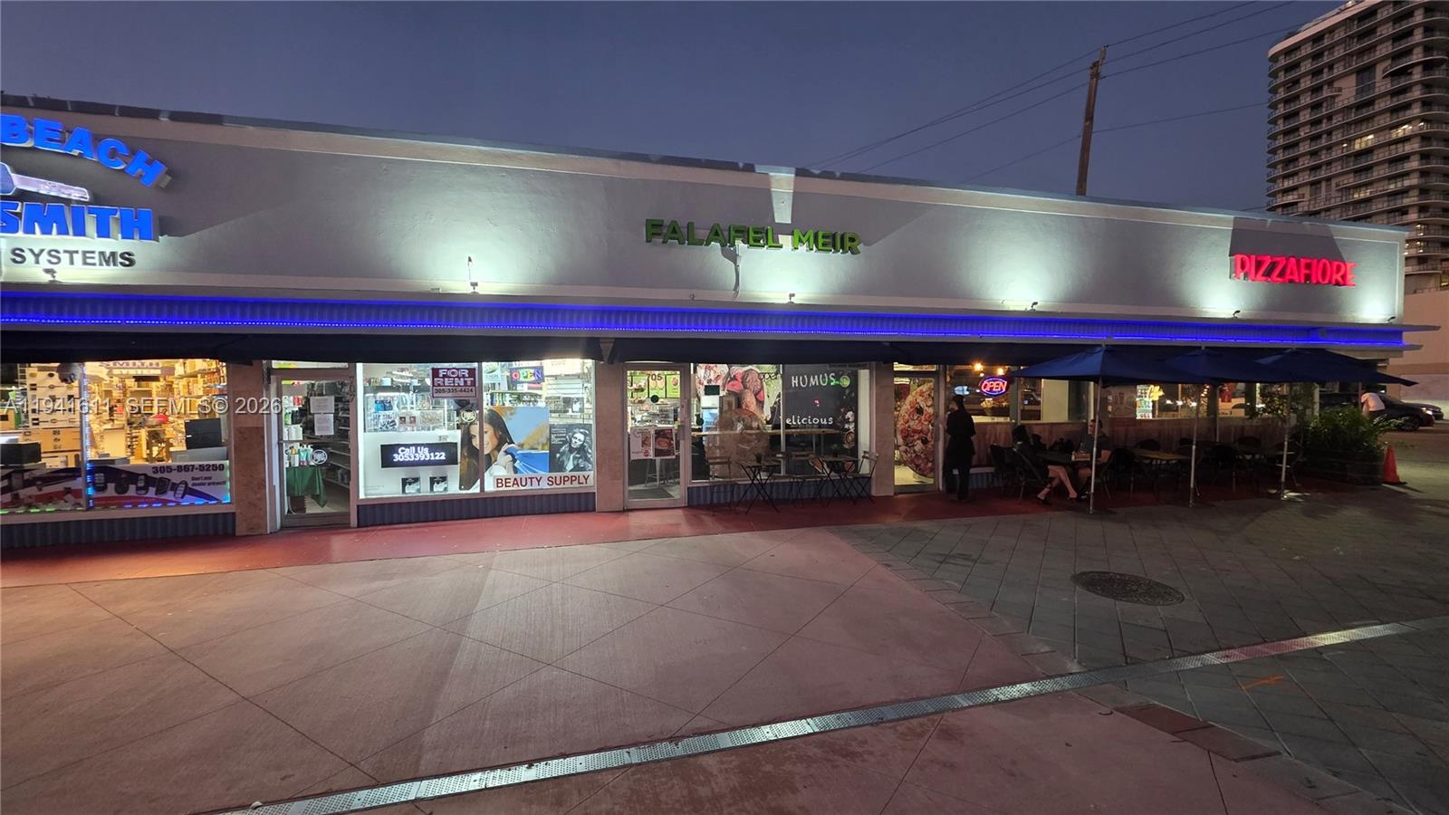 A street-level view of a commercial strip mall featuring several storefronts with signage at dusk — 707 71st St, Miami Beach FL 33141, MIAMI BEACH, FL