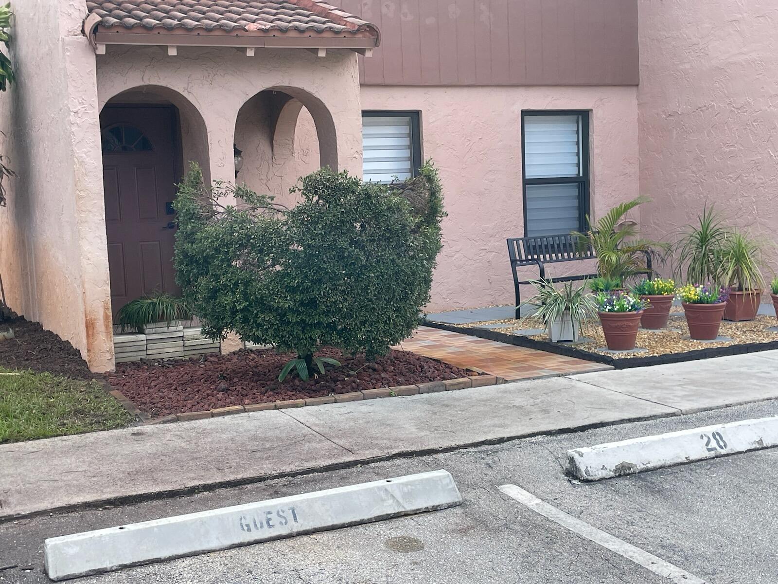 The exterior of a pink stucco building features a covered entryway and a small garden — 28 Madrid Lane, Davie FL 33324, DAVIE, FL