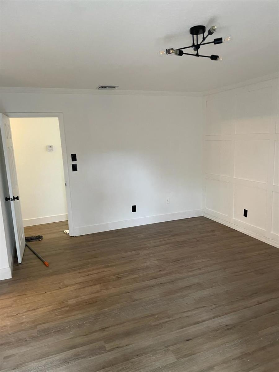 An empty room features white walls with wainscoting, wood-look flooring, and a modern light fixture — 28 Madrid Lane, Davie FL 33324, DAVIE, FL