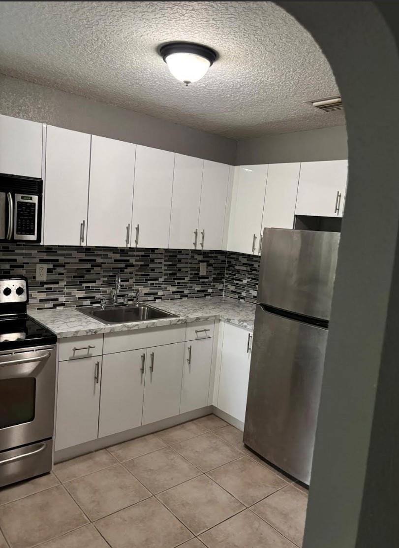 A kitchen with white cabinets, stainless steel appliances, a patterned backsplash, and light-colored countertops — 407 SE 3rd Avenue # B, Hallandale Beach FL 33009, HALLANDALE BEACH, FL