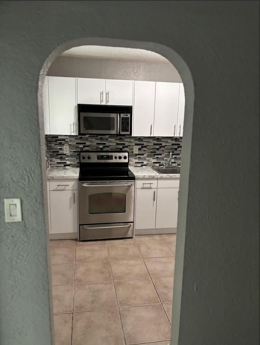 A view through an arched doorway into a kitchen with white cabinets and stainless appliances — 407 SE 3rd Avenue # B, Hallandale Beach FL 33009, HALLANDALE BEACH, FL