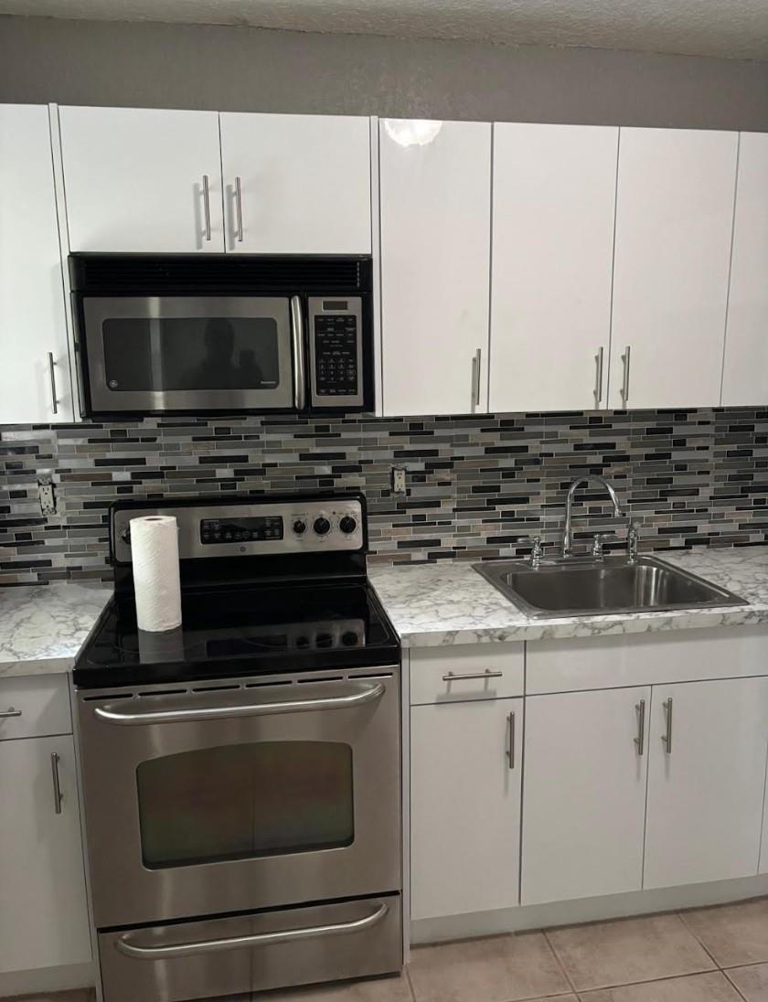 A kitchen with white cabinets, stainless steel appliances, a marble-patterned countertop, and a mosaic backsplash — 407 SE 3rd Avenue # B, Hallandale Beach FL 33009, HALLANDALE BEACH, FL