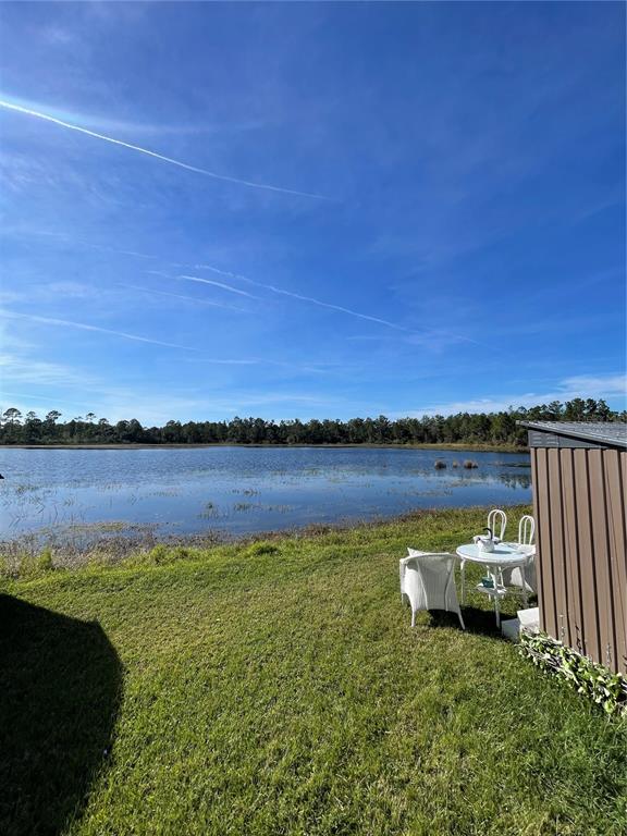 A small table and chairs sit on a grassy lawn overlooking a lake and forest — 57 KOVE BOULEVARD, OSTEEN, FL