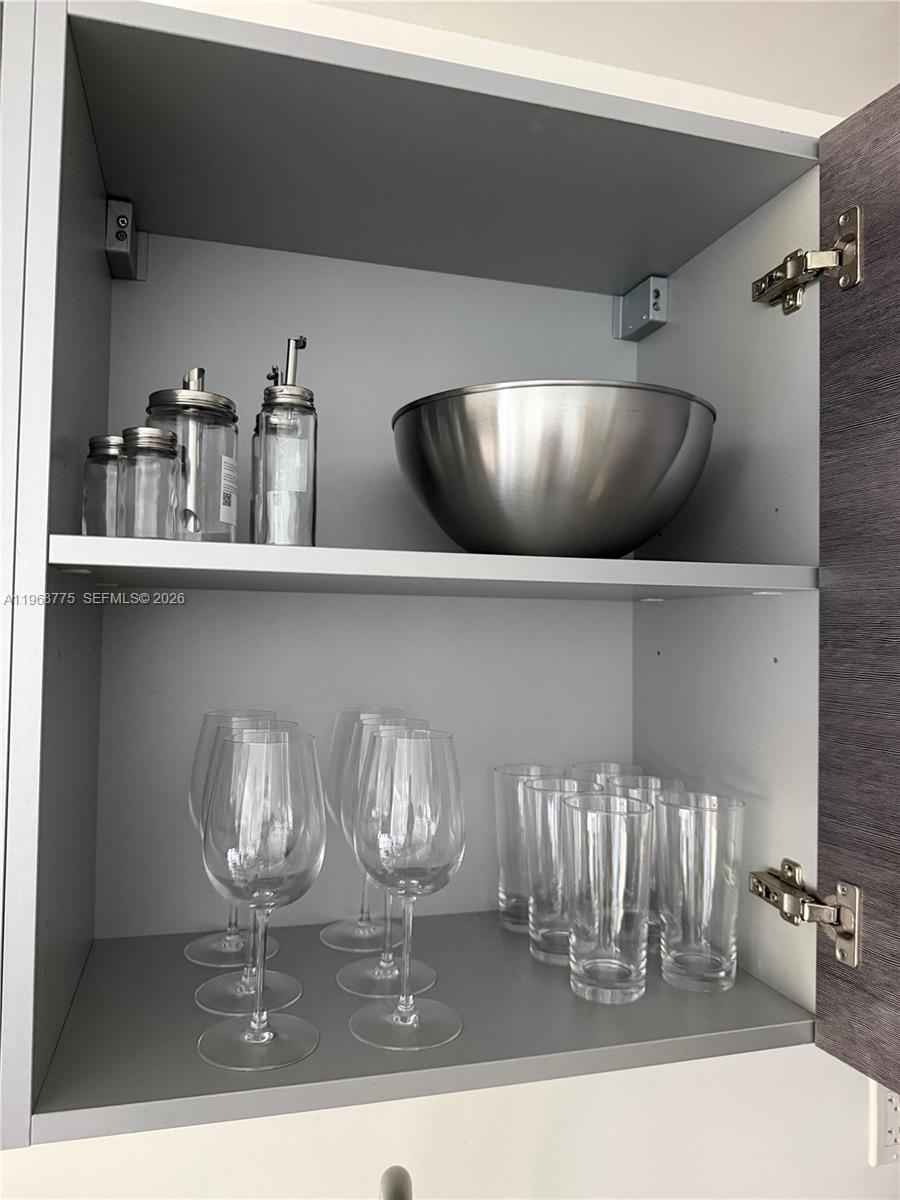 A kitchen cabinet contains a metal bowl, glass containers, wine glasses, and drinking glasses — 151 SE 1st St # 909, Miami FL 33131, MIAMI, FL