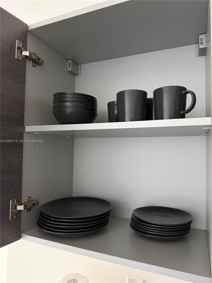 An open kitchen cabinet contains stacks of dark plates, bowls, and mugs on two shelves — 151 SE 1st St # 909, Miami FL 33131, MIAMI, FL