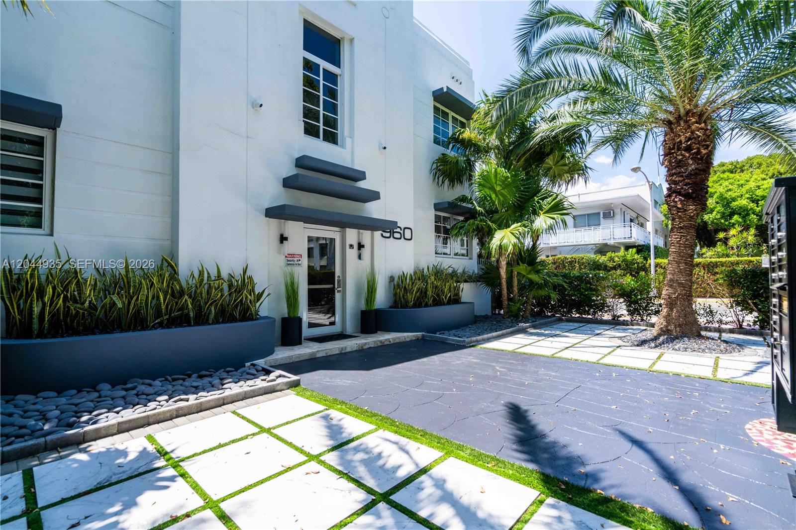 The exterior of a white building features a glass entrance door and a paved courtyard — 960 Jefferson Ave, Miami Beach FL 33139, MIAMI BEACH, FL