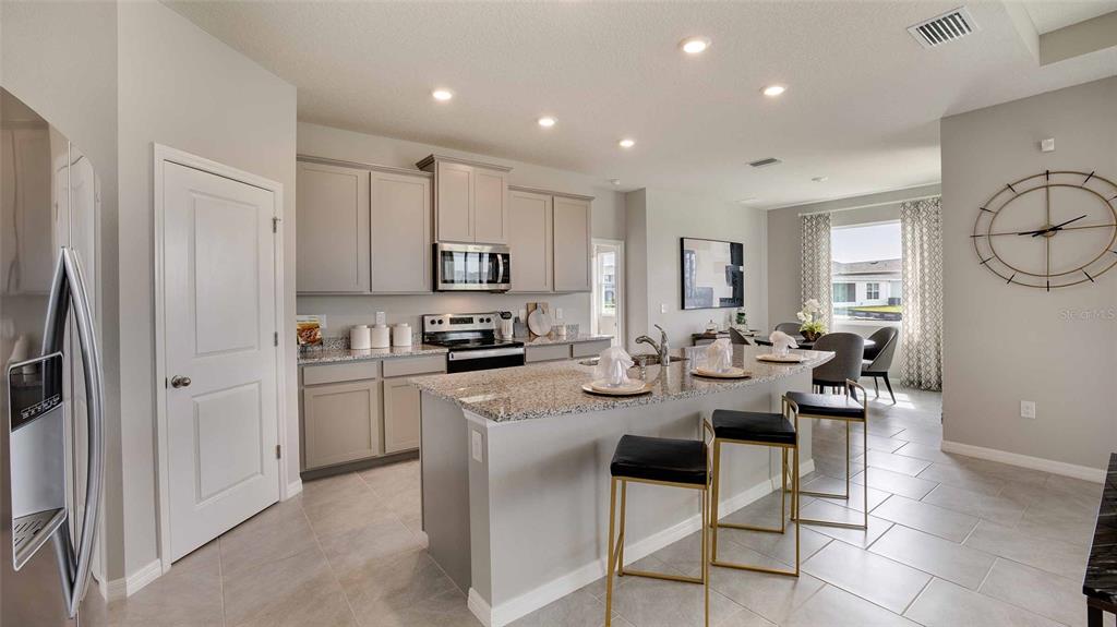 A kitchen features gray cabinets, granite countertops, a center island with bar stools, and tile flooring — 32693 DULUTH DRIVE, WESLEY CHAPEL, FL