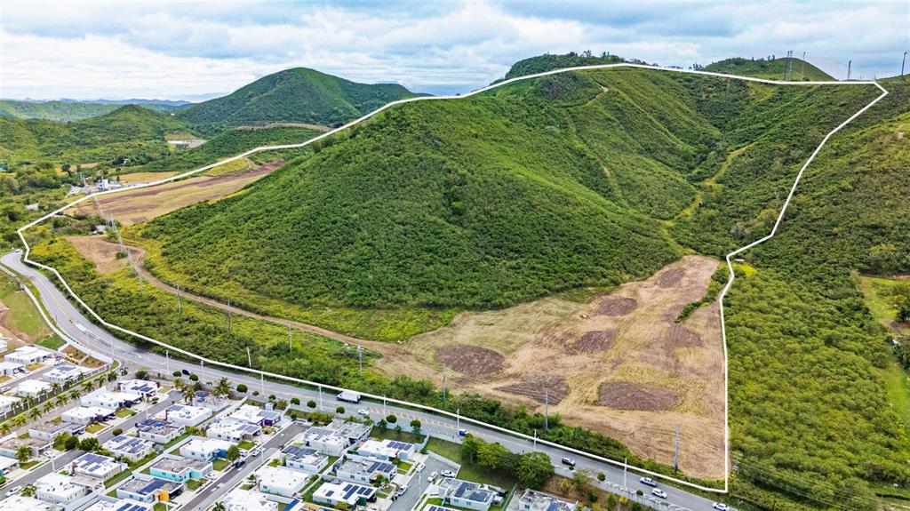 An aerial view shows a large, hilly plot of land outlined in white near houses — PR-153 KM 10.7 BO. RIO JUEYES, SANTA ISABEL, PR