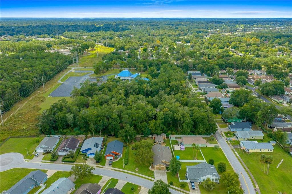 An aerial view shows a suburban neighborhood with houses, dense trees, and a blue-roofed building — 4016 NE 23RD PLACE, OCALA, FL