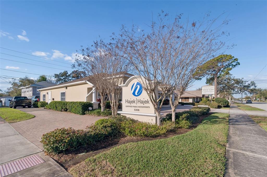 A beige office building with a prominent sign for Hajek & Hajek stands near a sidewalk — 5308 CENTRAL AVENUE, ST PETERSBURG, FL