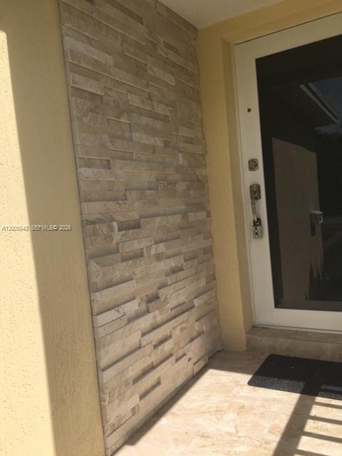 A stone-tiled accent wall stands next to a white front door on a porch — 805 NE 138th St, North Miami FL 33161, NORTH MIAMI, FL