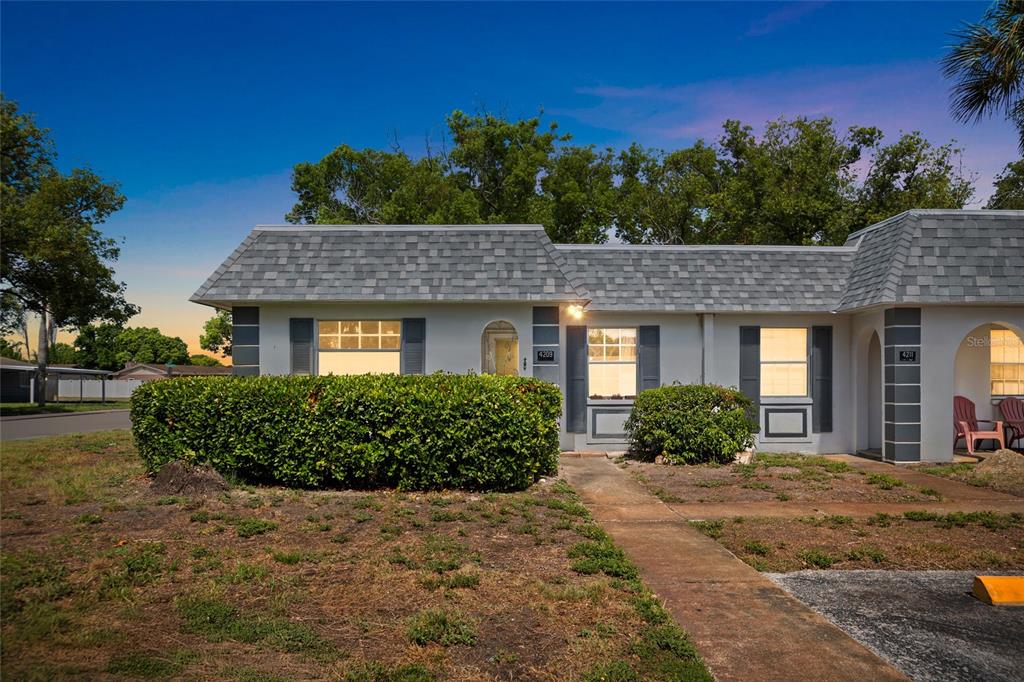 A single-story duplex with gray shingled roofs, white exterior walls, and a front hedge — 4209 REDCLIFF PLACE, NEW PORT RICHEY, FL