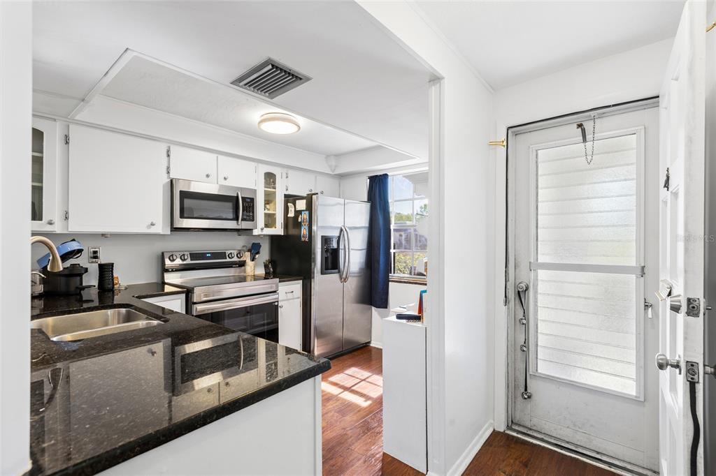 A kitchen with white cabinets, black countertops, stainless steel appliances, and an adjacent exterior door — 4209 REDCLIFF PLACE, NEW PORT RICHEY, FL
