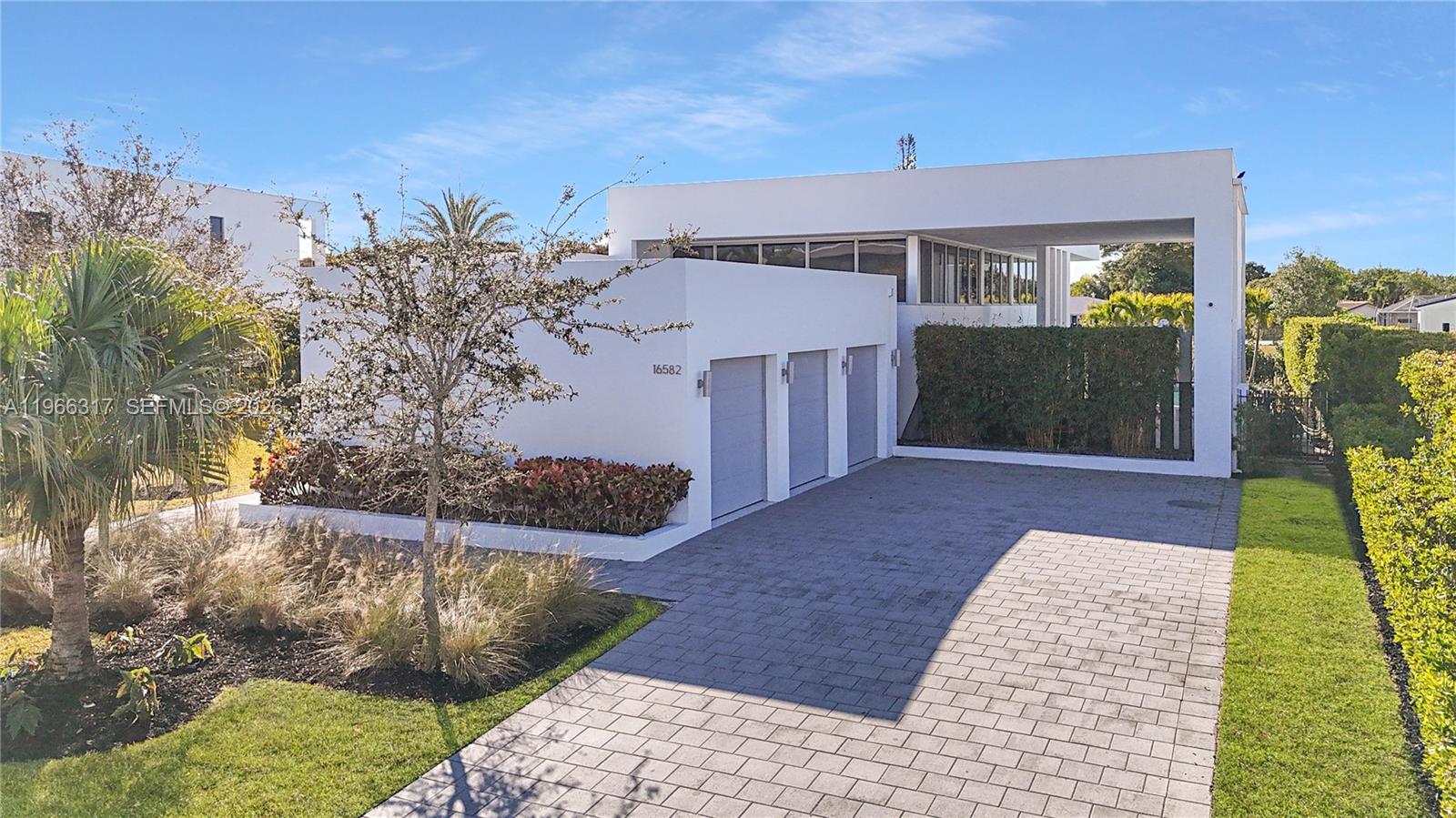 A modern white house features a three-car garage and a paved driveway — 16582 S Botaniko Dr S, Weston FL 33326, WESTON, FL