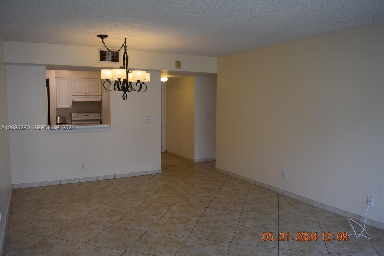 An empty room features beige tiled floors, a chandelier, and an open kitchen pass-through — DANIA BEACH, FL