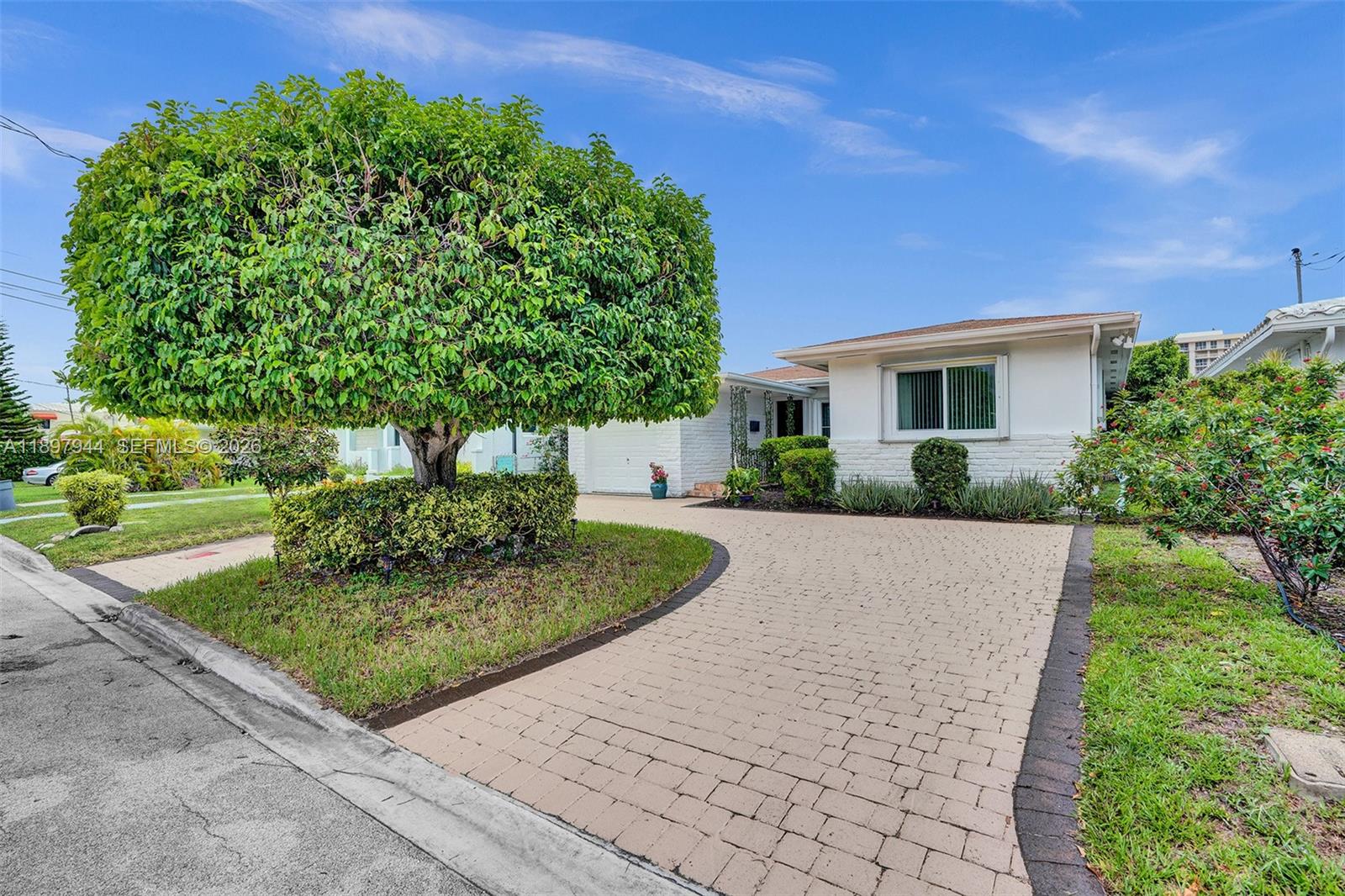 A white single-story house features a paved driveway and a large, manicured tree — 8851 Byron Ave, Surfside FL 33154, SURFSIDE, FL
