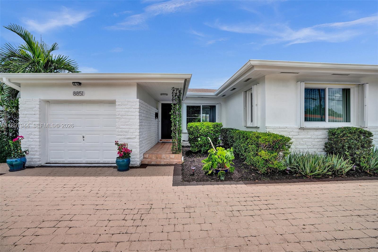 The exterior of a white, single-story house features a brick driveway and a garage — 8851 Byron Ave, Surfside FL 33154, SURFSIDE, FL