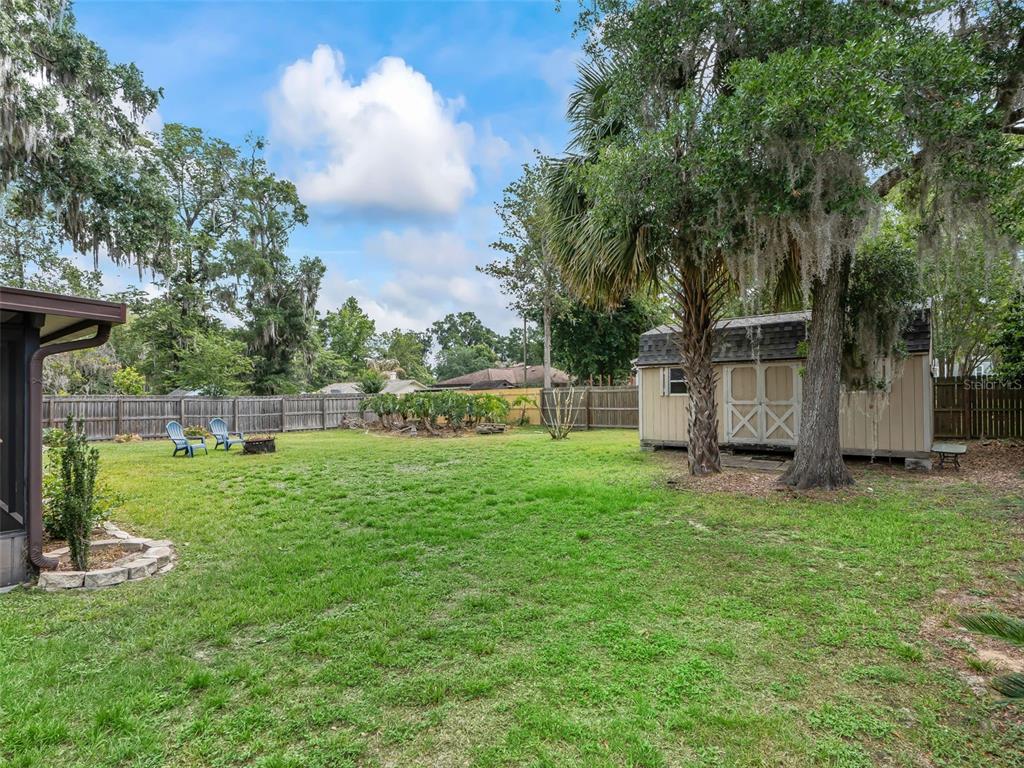 A grassy backyard features a wooden storage shed, mature trees, and a wooden privacy fence — 5073 SE 33RD TERRACE, OCALA, FL