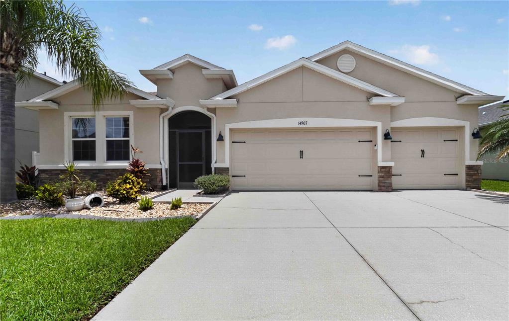 A single-story house with a beige stucco exterior, a three-car garage, and a concrete driveway — 14907 TRINITY FALL WAY, BRADENTON, FL