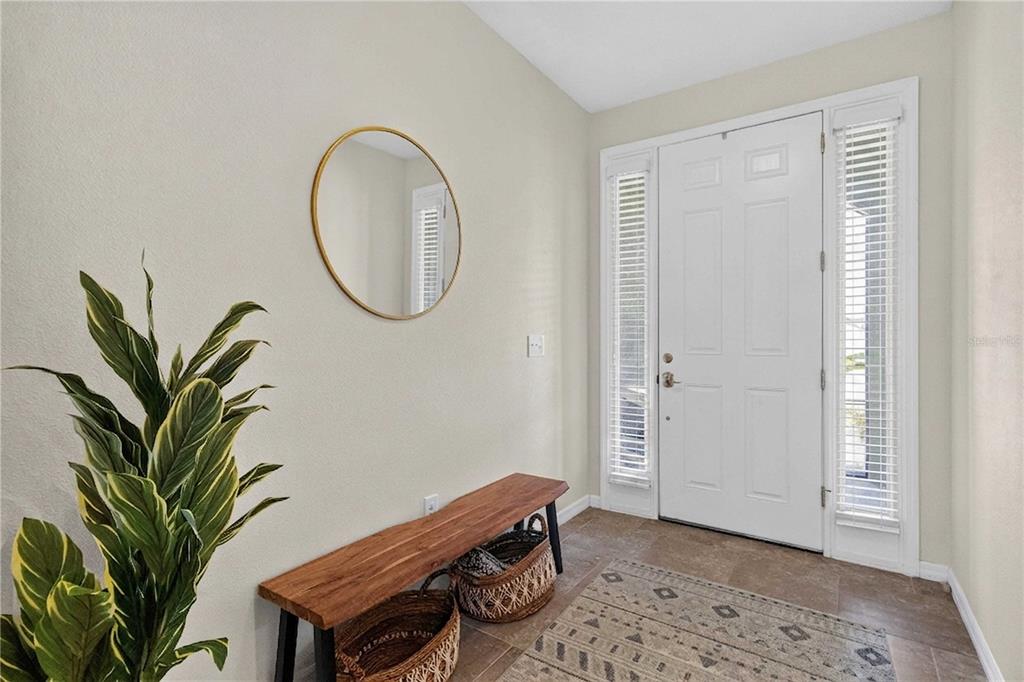 A bright entryway features a wooden bench, a round mirror, and a potted plant — 14907 TRINITY FALL WAY, BRADENTON, FL