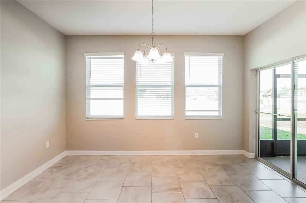 A dining area with tile flooring, a central chandelier, three windows, and a sliding glass door — 2344 CRESCENT MOON STREET, KISSIMMEE, FL
