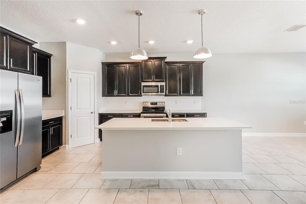 A kitchen features dark wood cabinets, stainless steel appliances, a white island, and tile flooring — 2344 CRESCENT MOON STREET, KISSIMMEE, FL