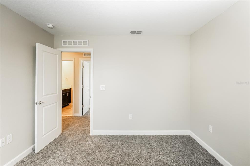 A carpeted bedroom features light gray walls, a white door, and an open doorway — 2344 CRESCENT MOON STREET, KISSIMMEE, FL