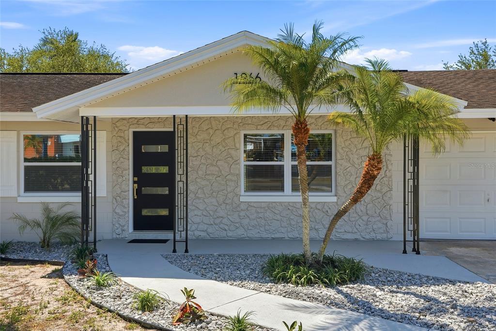The exterior of a single-story house features a stone facade, a black door, and palm trees — 1966 119TH STREET, LARGO, FL
