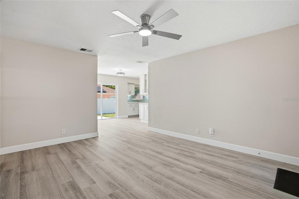 A living room with light wood-look flooring and a ceiling fan leads to a kitchen — 1966 119TH STREET, LARGO, FL