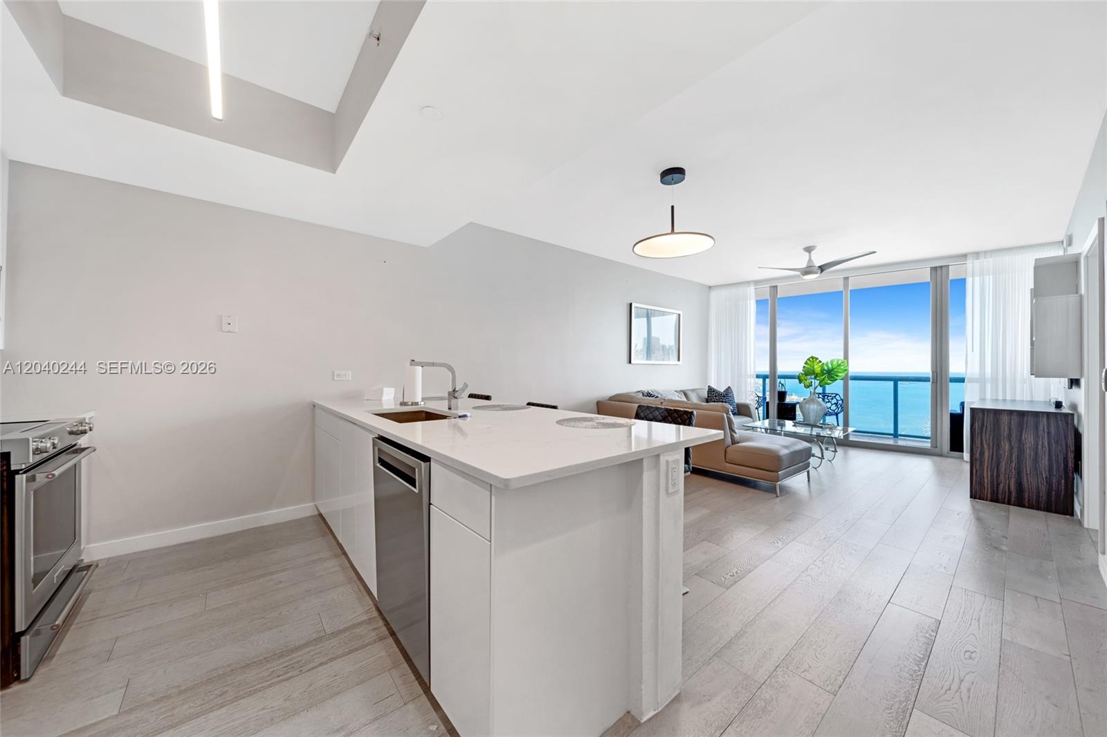 A modern kitchen with white cabinetry and an island overlooks a living area with ocean views — 888 Biscayne Blvd # 3907, Miami FL 33132, MIAMI, FL