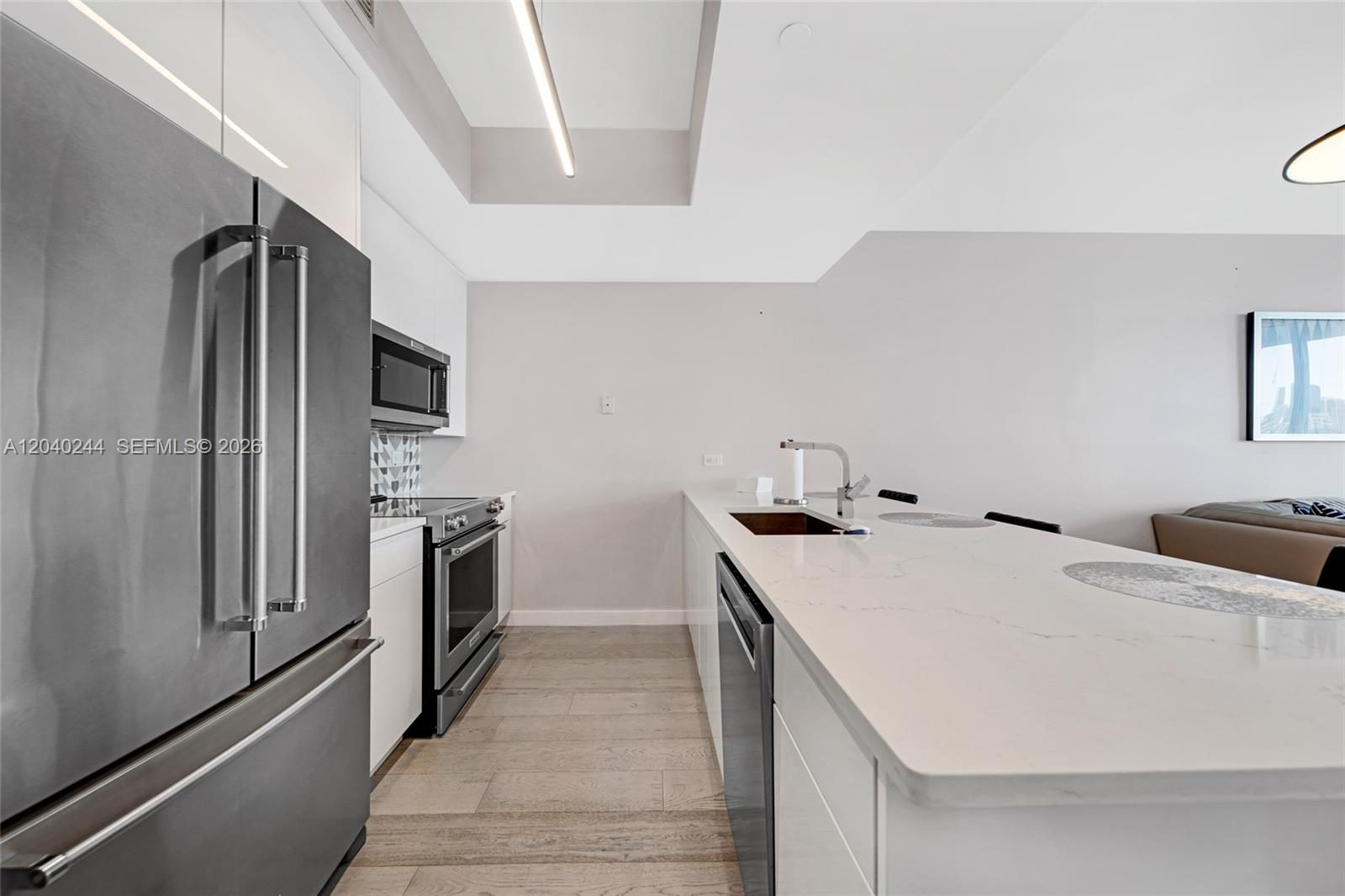 A modern kitchen features white cabinetry, stainless steel appliances, and a large quartz island — 888 Biscayne Blvd # 3907, Miami FL 33132, MIAMI, FL