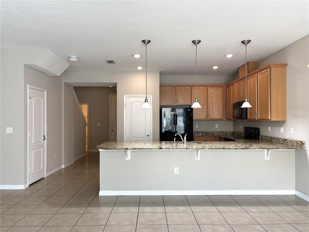 A kitchen features a granite breakfast bar, light wood cabinets, and tile flooring — 5110 ADELAIDE DRIVE, KISSIMMEE, FL