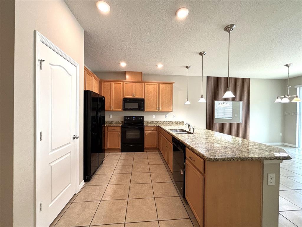 A kitchen features light wood cabinets, granite countertops, black appliances, and a large island — 5110 ADELAIDE DRIVE, KISSIMMEE, FL