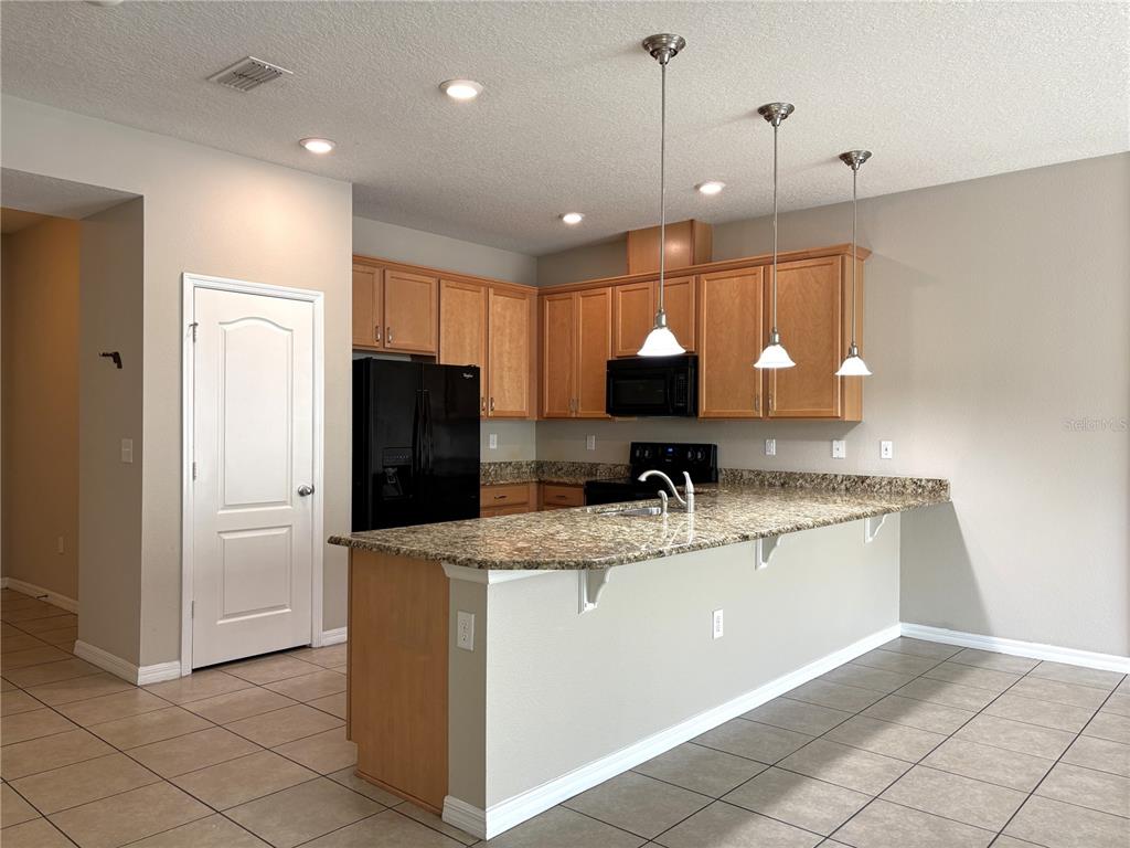A kitchen features light wood cabinets, granite countertops, a black refrigerator, and three pendant lights — 5110 ADELAIDE DRIVE, KISSIMMEE, FL
