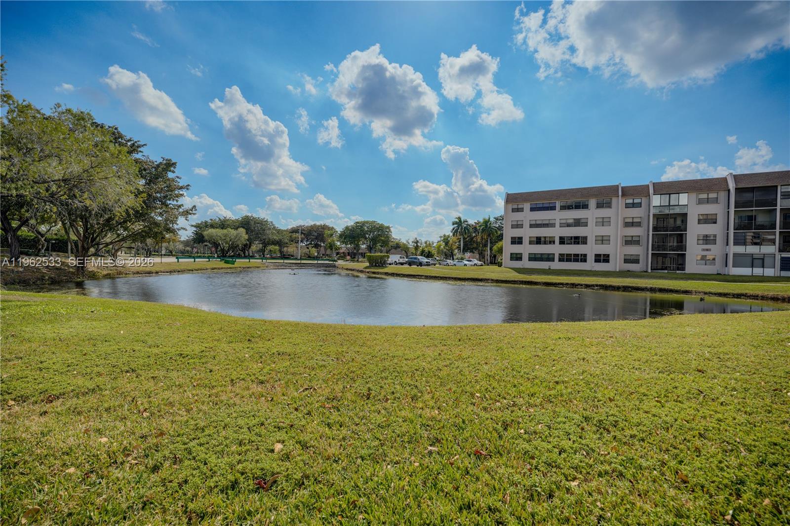 A multi-story apartment building sits beside a pond surrounded by a grassy lawn — 2901 N Nob Hill Rd # 303, Sunrise FL 33322, SUNRISE, FL