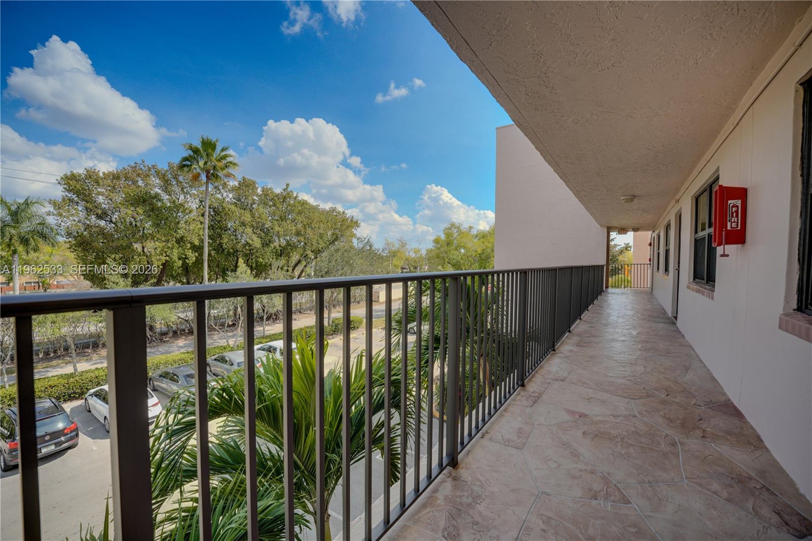 An outdoor balcony with a metal railing overlooks a parking lot and palm trees — 2901 N Nob Hill Rd # 303, Sunrise FL 33322, SUNRISE, FL
