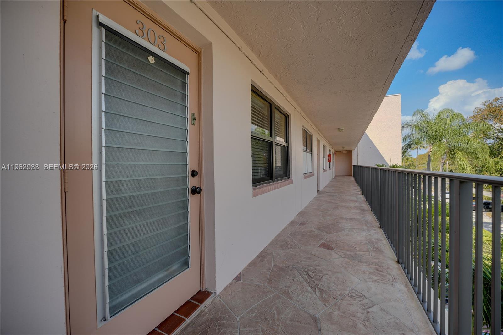 An exterior walkway features a light-colored door labeled 303, windows, and a metal railing — 2901 N Nob Hill Rd # 303, Sunrise FL 33322, SUNRISE, FL