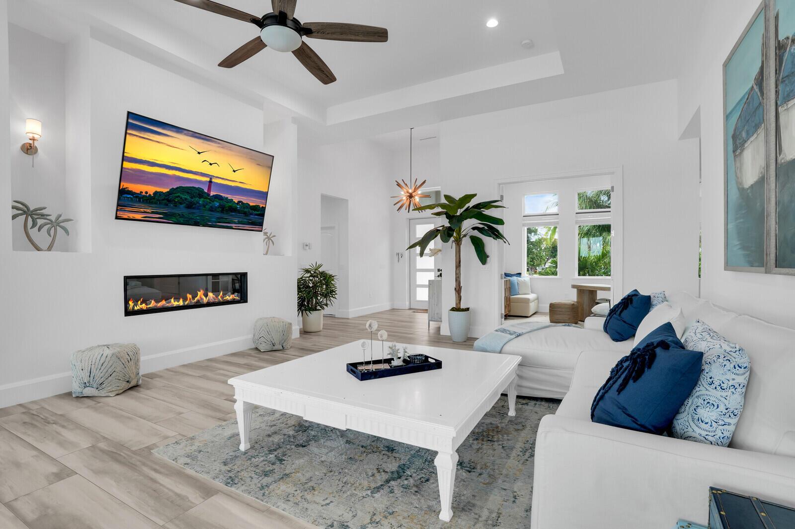 A bright living room features a fireplace, wall-mounted television, white sofa, and wood-look flooring — 974 Marlin Drive, Jupiter FL 33458, JUPITER, FL