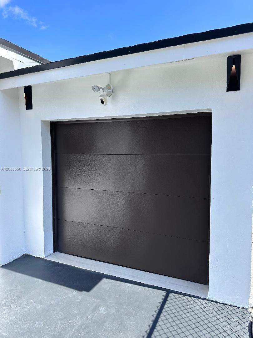 A modern garage door is set into a white exterior wall with a security camera — 2750 Washington St # 0, Hollywood FL 33020, HOLLYWOOD, FL