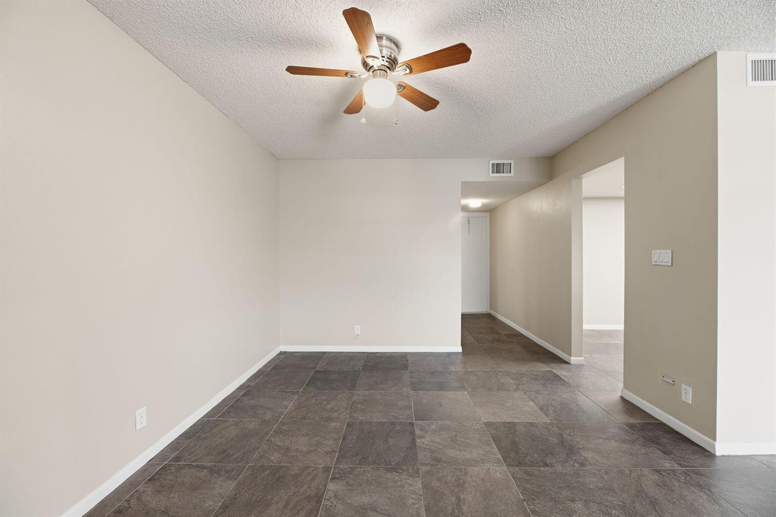 An empty room features dark tile flooring, beige walls, and a ceiling fan — 1769 NE 40th Place # 506, Pompano Beach FL 33064, POMPANO BEACH, FL