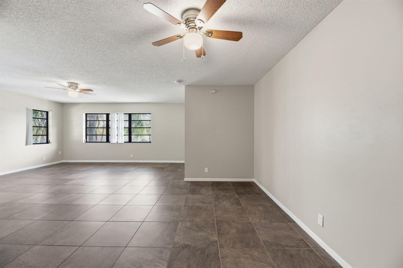An empty room with large dark floor tiles, two ceiling fans, and multiple windows — 1769 NE 40th Place # 506, Pompano Beach FL 33064, POMPANO BEACH, FL