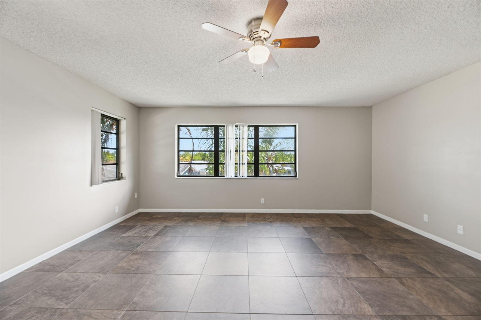 An empty room with large dark floor tiles, light gray walls, and a ceiling fan — 1769 NE 40th Place # 506, Pompano Beach FL 33064, POMPANO BEACH, FL